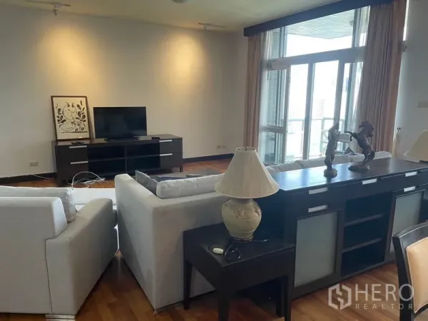 Condominium for rent in Pathum Wan, Bangkok - Lounge setup with sofas facing TV console beside floor-to-ceiling balcony doors.