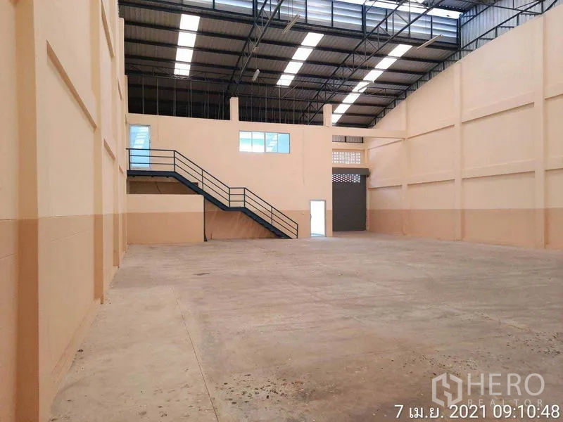 工厂 出租在Bang Bua Thong, Nonthaburi - 仓库视角展示钢桁架屋顶、夹层楼梯和装卸卷帘门。