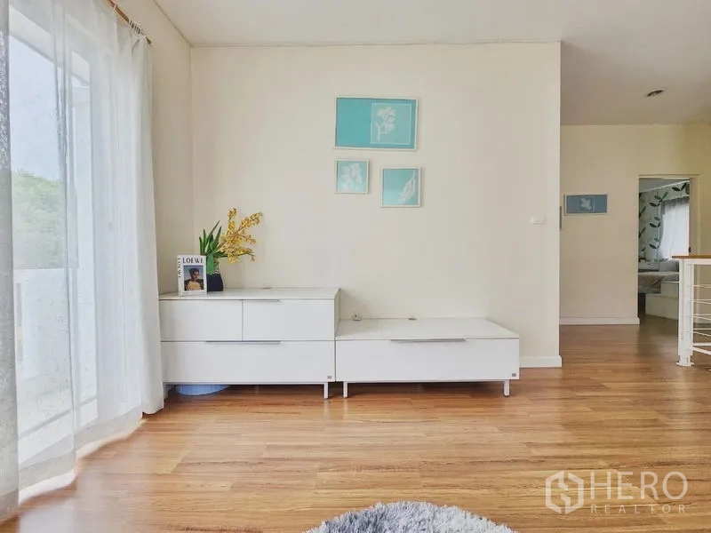 Detached House for rent in Prawet, Bangkok - Upstairs landing with low storage cabinet, balcony curtains and framed art.