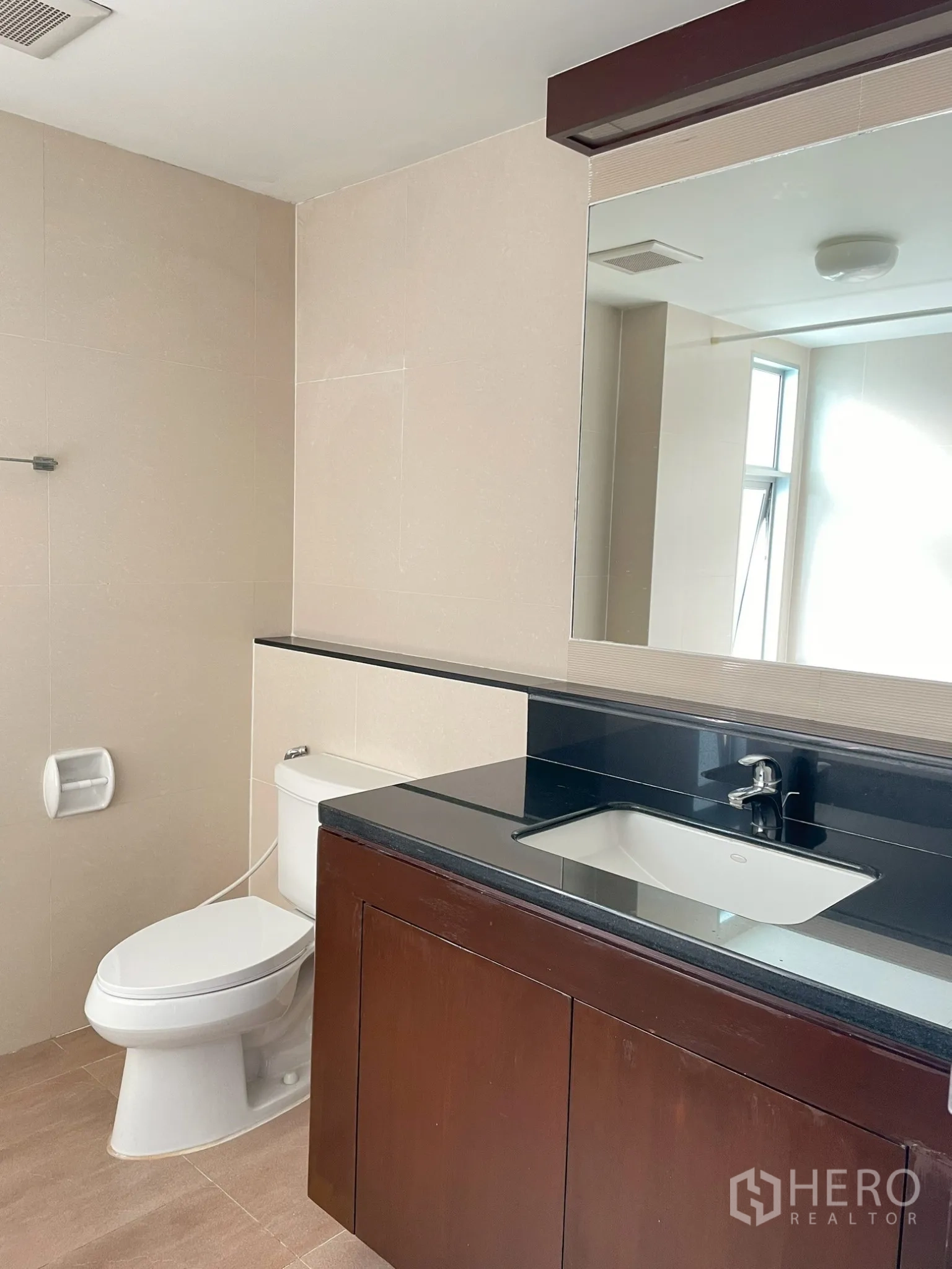 Apartment for rent in Khlong Toei, Bangkok - Second bathroom with wide mirror, dark countertop, and toilet.