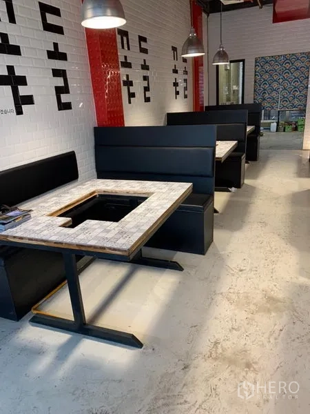 Shophouse for rent in Khlong Toei, Bangkok - Row of black booths with pendant lighting and tables featuring grill cut-outs along white tiled walls.