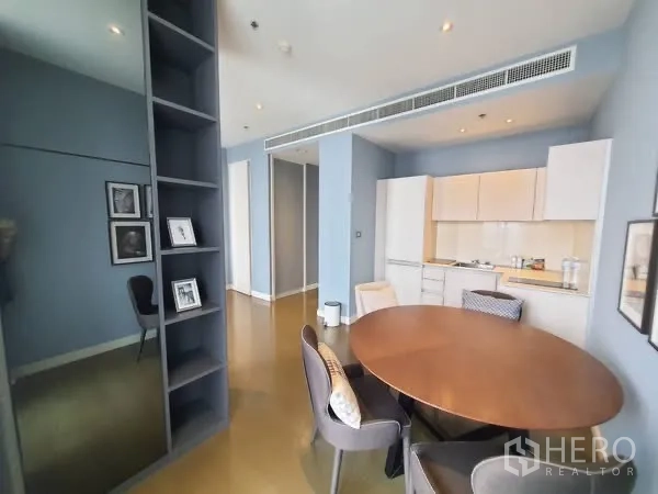 Condominium for rent in Pathum Wan, Bangkok - Compact white kitchen with built-in cabinets next to a cozy dining nook and shelving unit.