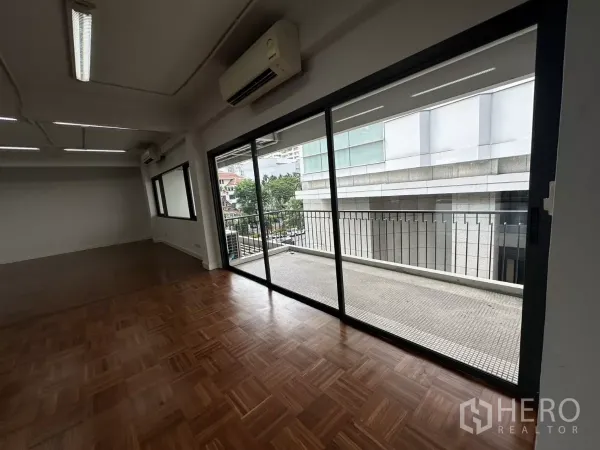 Office Space for rent in Watthana, Bangkok - Office corner showing sliding glass doors to the balcony and view of neighboring buildings.