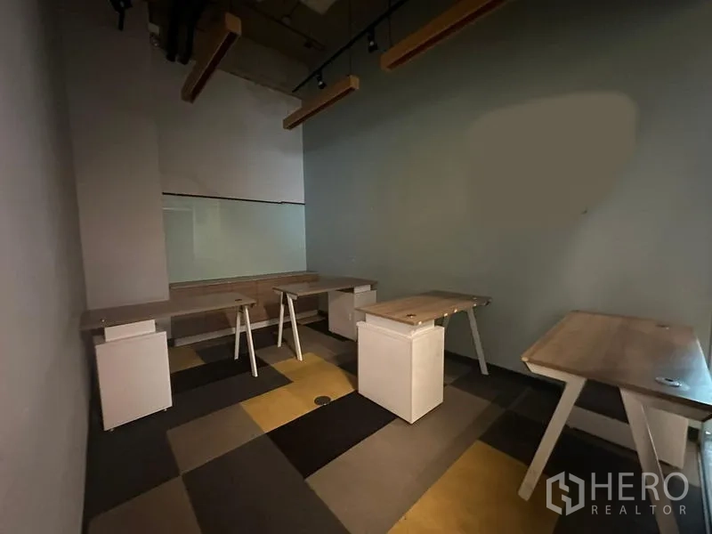 Office Space for rent - Workroom with built-in desks, track lights and a glass partition.