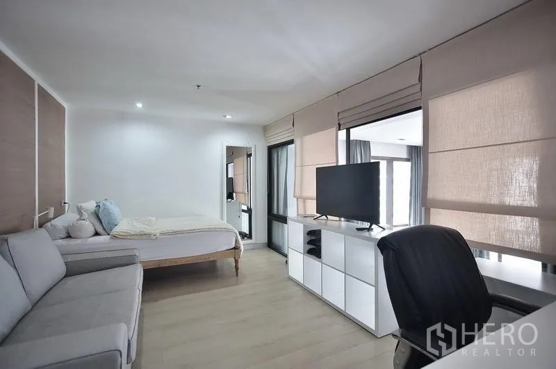 Condominium for rent in Khlong Toei, Bangkok - Upper-level bedroom with sofa, large windows with blinds, TV console and light wood flooring.