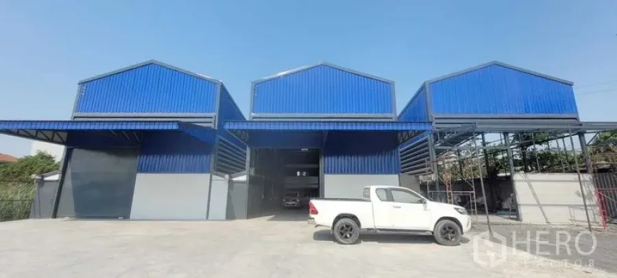 Warehouse for rent in Prawet, Bangkok - Front elevation of three-bay blue warehouse with large roller doors and concrete yard.