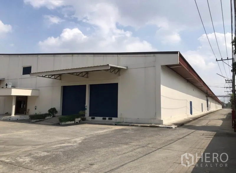 Warehouse for rent in Lam Luk Ka, Pathum Thani - Front facade with twin blue roller doors and a canopy for truck loading.