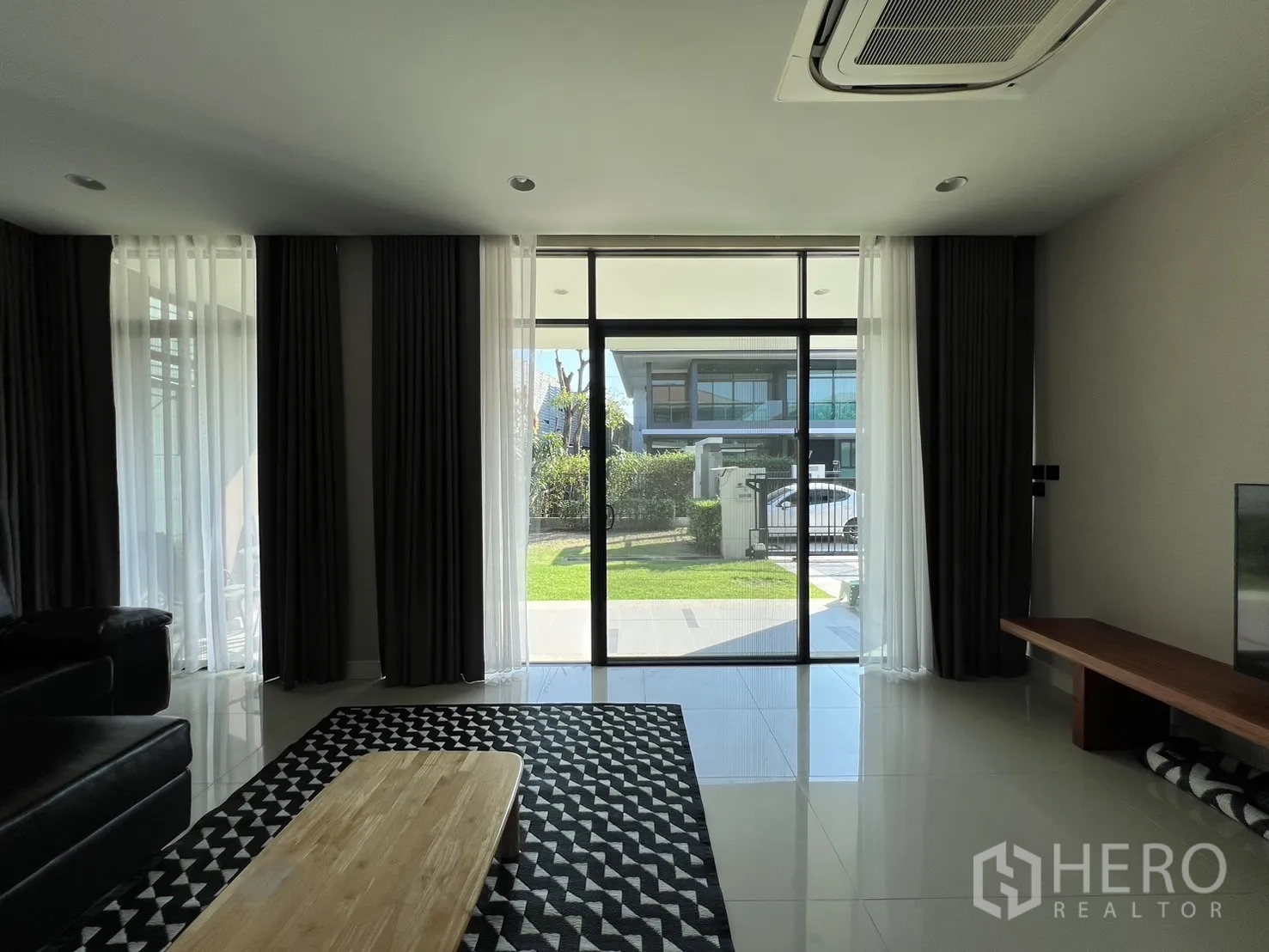 Detached House for rent or sale in Bang Kapi, Bangkok - Living area opening to patio through floor‑to‑ceiling glass, bringing in natural light and greenery.