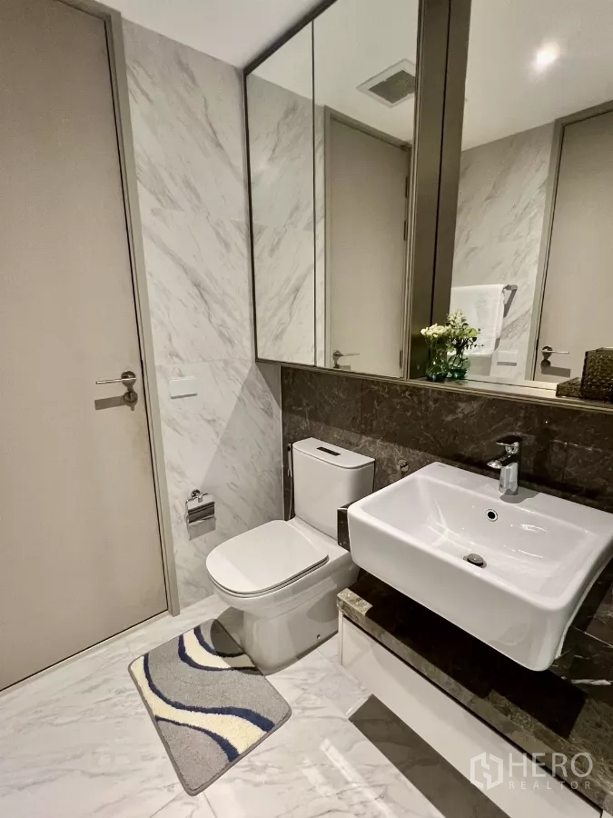 Condominium for rent in Khlong Toei, Bangkok - Modern bathroom with marble tiles, wide mirror, toilet and square basin.