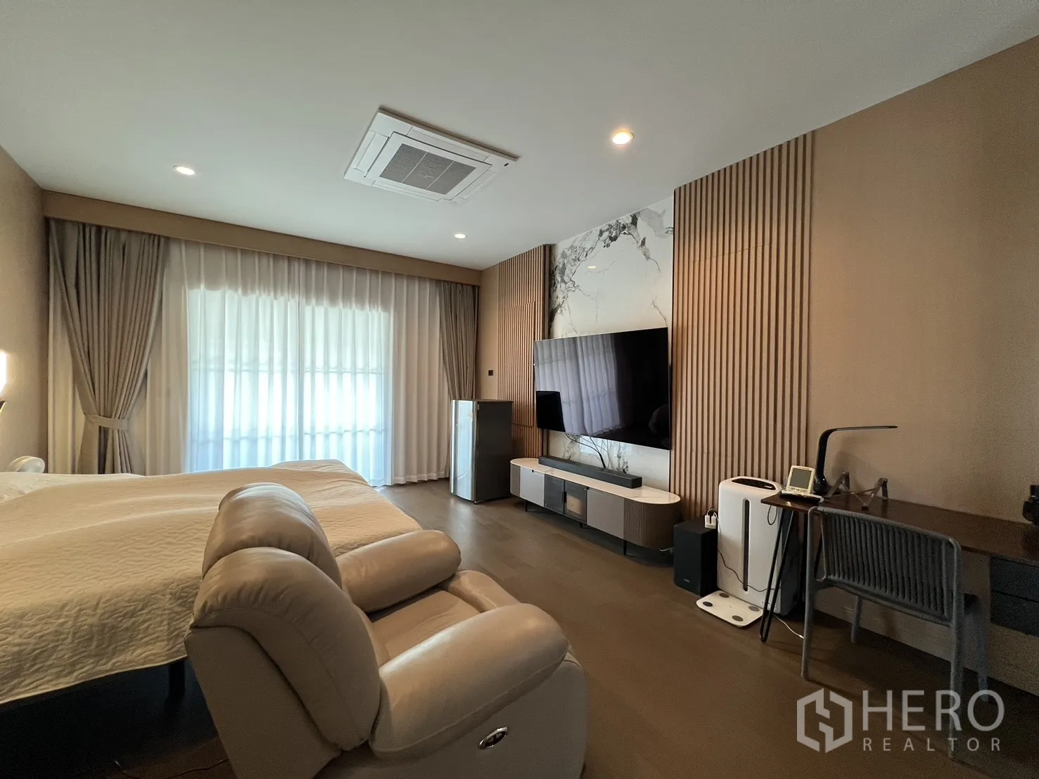 Detached House for rent or sale in Mueang Pathum Thani, Pathum Thani - Spacious master bedroom with lounge chairs, TV wall and full-height curtains.