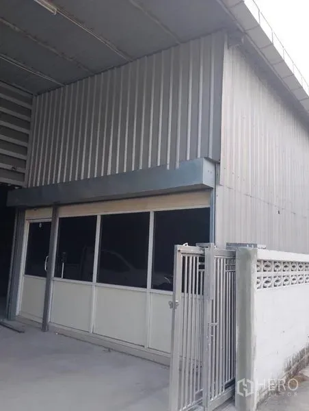 Warehouse for rent in Huai Khwang, Bangkok - Front office-style entrance with sliding glass doors beside a metal gate under the warehouse canopy.