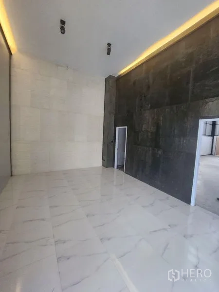 Warehouse for rent or sale in Lam Luk Ka, Pathum Thani - High-ceiling lobby or showroom with white marble-look flooring, a dark feature wall and recessed LED lighting.