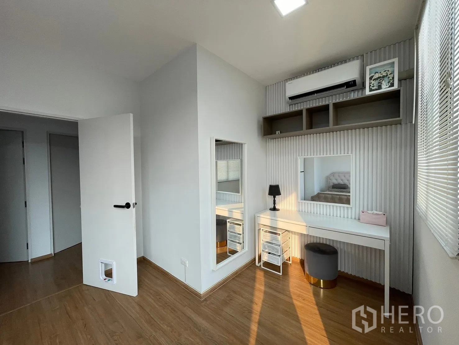 Townhouse for rent in Bang Phli, Samut Prakan - Secondary bedroom with a makeup desk, large mirror, wall shelves, and air conditioner.
