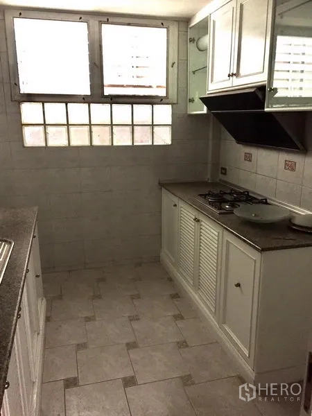 Townhouse for rent in Watthana, Bangkok - Fitted kitchen with white cabinets, gas cooktop, range hood and small windows.