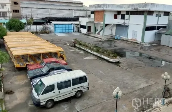 Factory for sale in Bang Phli, Samut Prakan - Elevated view of the spacious concrete yard with parked vehicles and a long covered structure.