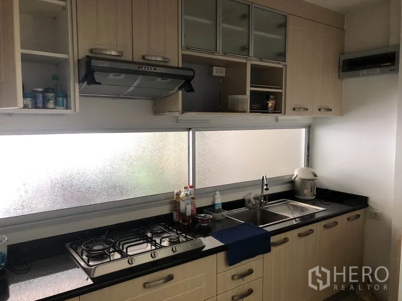 Townhouse for rent or sale in Suan Luang, Bangkok - Suan Luang townhouse kitchen with built-in light-wood cabinets, gas hob, range hood and long black countertop under frosted windows.