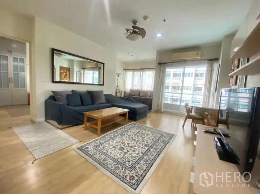 Condominium for rent in Bang Kapi, Bangkok - Spacious living area with L-shaped sofa, rug, TV and sliding doors to the balcony.