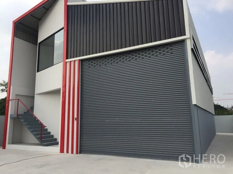 Warehouse for sale in Khlong Luang, Pathum Thani - Modern warehouse facade with wide roller shutter and bold red frame.