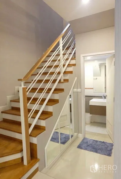 Detached House for rent in Suan Luang, Bangkok - Wood staircase with white balustrade, under-stairs mirrored storage, and entry to a guest bathroom.
