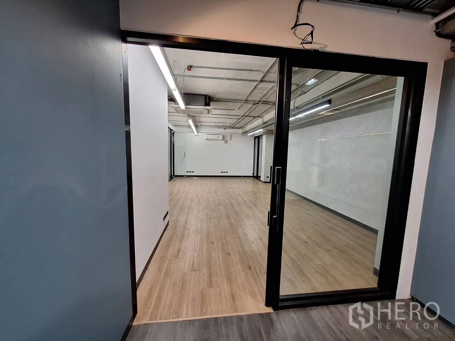 Office Space for rent - Entry through black-framed sliding glass doors to a light wood floor office.