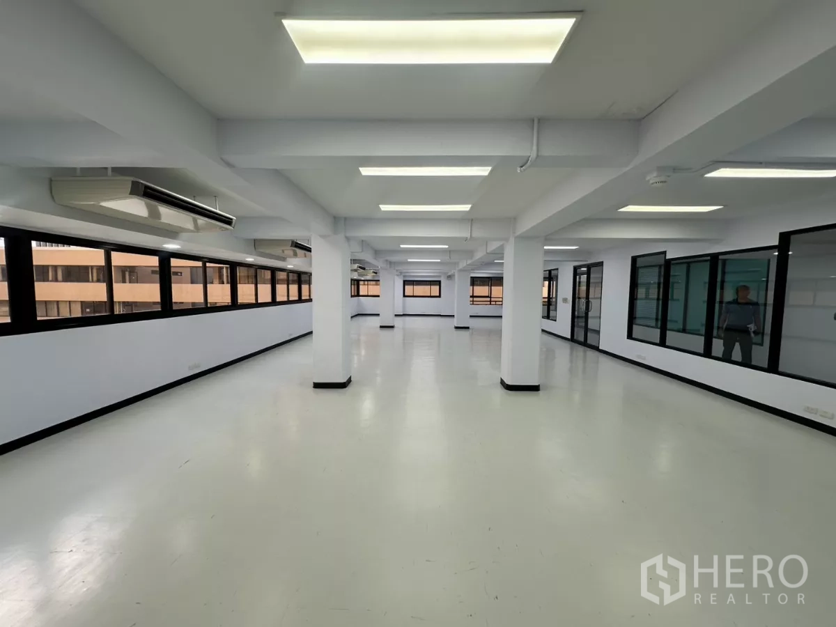 Office Space for rent - Bright office interior with continuous windows on one side, glass-partition rooms on the other and ceiling AC units.