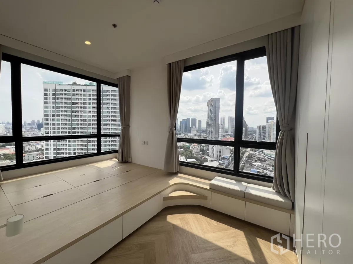 Condominium for rent or sale in Chatuchak, Bangkok - Corner bedroom with panoramic windows, platform bed with storage and window bench facing the skyline.