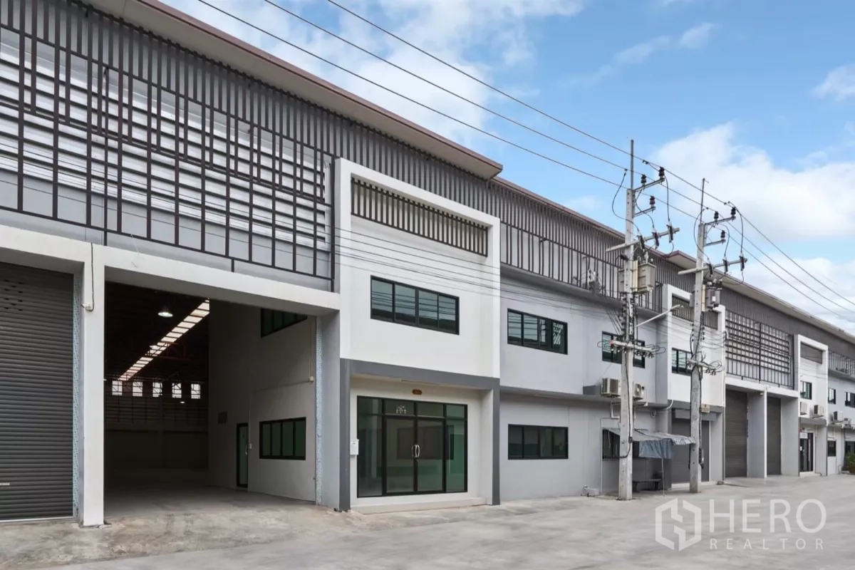 Factory for rent in Mueang Samut Sakhon, Samut Sakhon - Row of factory units with high roller shutters and a wide driveway, one bay open.