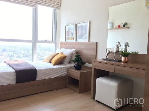 Condominium for rent in Khlong Toei, Bangkok - Sunlit second bedroom with single bed, floor‑to‑ceiling windows, city views and a wooden dressing table.