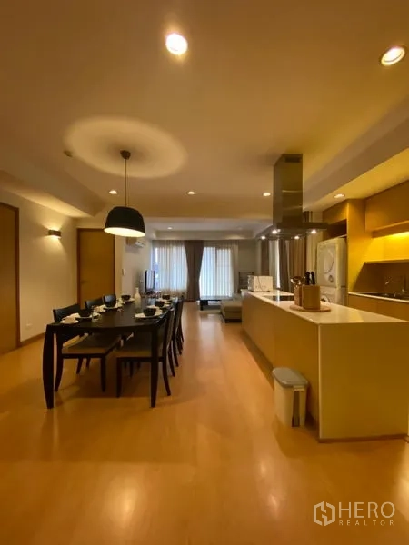 Condominium for rent in Watthana, Bangkok - Open-plan dining area with a six-seat table beside a modern island kitchen under warm lighting.
