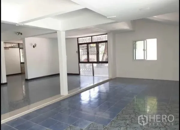 Detached House for rent in Lat Phrao, Bangkok - Spacious open‑plan ground floor with mixed tile flooring, white columns and windows with security grilles.