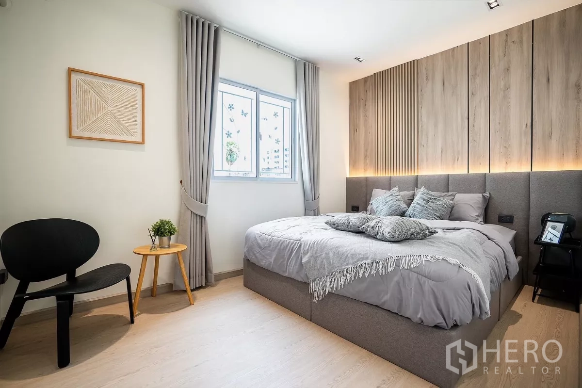 Detached House for rent in Huai Khwang, Bangkok - Spacious bedroom with feature wall, accent chair and grey drapes.