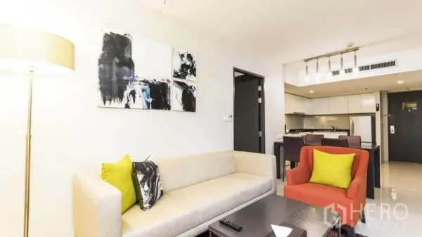 房间 出租在Watthana, Bangkok - 起居区配沙发、装饰画与落地灯，连接餐区与厨房。