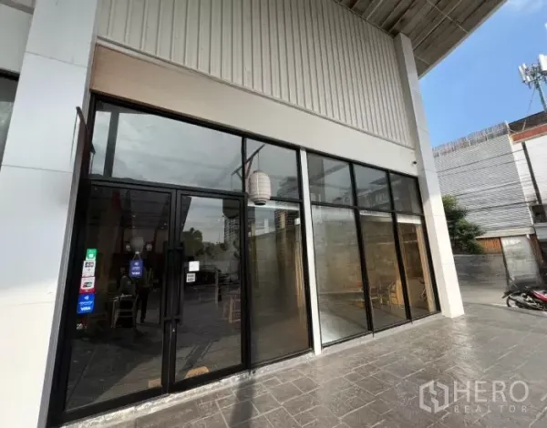 零售空间 出租在Watthana, Bangkok - 主入口为黑框玻璃门，连续高窗面向铺装步道。