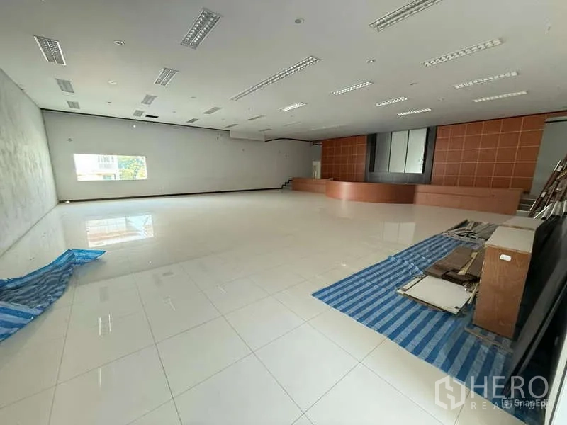 Warehouse for rent in Mueang Samut Prakan, Samut Prakan - Spacious tiled hall with drop ceiling lights and a wooden stage backdrop.