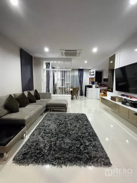 Detached House for rent - Open-plan lounge with TV wall, large rug and full-length curtains.