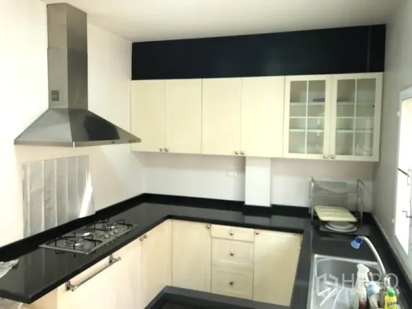 Detached House for rent or sale in Bang Kapi, Bangkok - U-shaped kitchen with black granite countertops, gas hob and stainless steel hood.