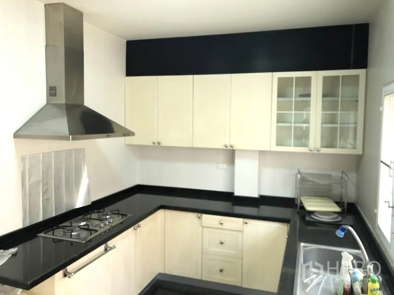 Detached House for rent or sale in Bang Kapi, Bangkok - U-shaped kitchen with black granite countertops, gas hob and stainless steel hood.