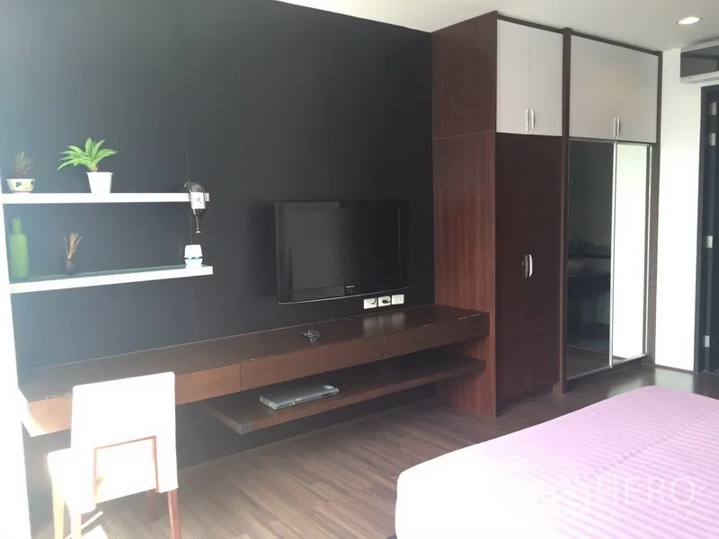 Condominium for rent in Khlong Toei, Bangkok - Bedroom with TV wall, work desk and built-in wardrobes with shelving.