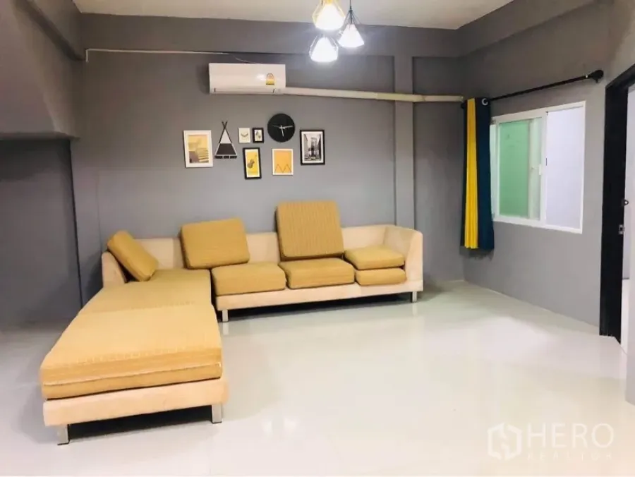 联排别墅 出租或出售在Huai Khwang, Bangkok - 宽敞客厅，L形沙发、灰色墙面、空调与墙面装饰画。