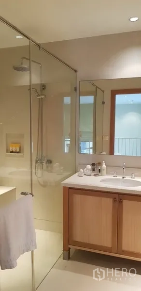 Condominium for rent in Khlong Toei, Bangkok - Modern bathroom with glass-enclosed rain shower and vanity cabinet.