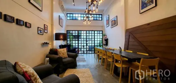 Townhouse for rent in Khlong Toei, Bangkok - Wide view of double-height living room with industrial chandelier, gallery wall and polished concrete floors.