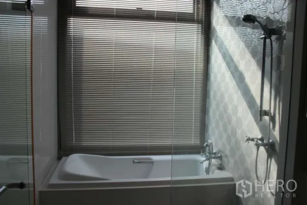 Condominium for rent or sale in Khlong Toei, Bangkok - Modern bathroom with separate bathtub, glass shower enclosure and window blinds.