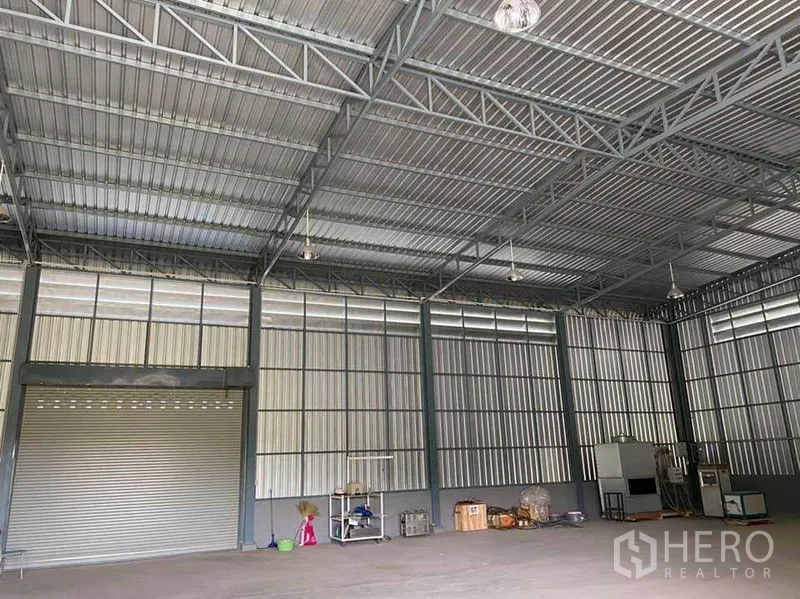 Warehouse for rent in Sam Phran, Nakhon Pathom - Roller shutter loading door with open floor space, industrial lighting and steel framing.