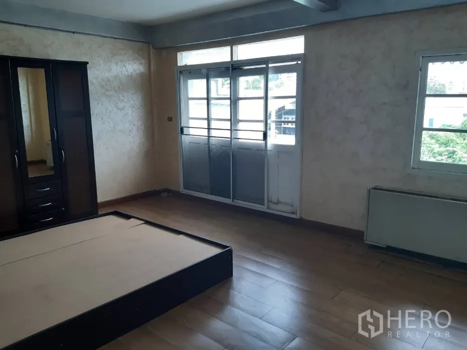 Townhouse for rent in Khlong Toei, Bangkok - Bedroom opening to a balcony through sliding doors with wood‑look floors.