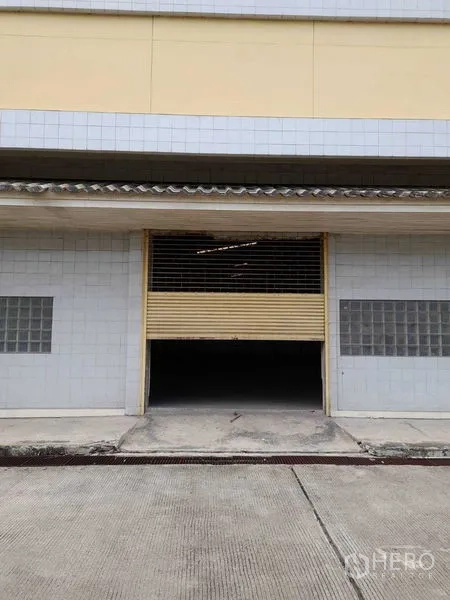 Warehouse for rent in Yan Nawa, Bangkok - Warehouse exterior with partially opened roller shutter and loading ramp at street level.