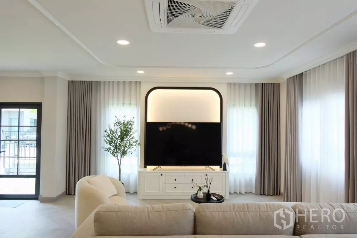 Detached House for sale in Bang Phli, Samut Prakan - Living room with recessed TV feature wall, cassette air-conditioner, sheer curtains and a potted plant