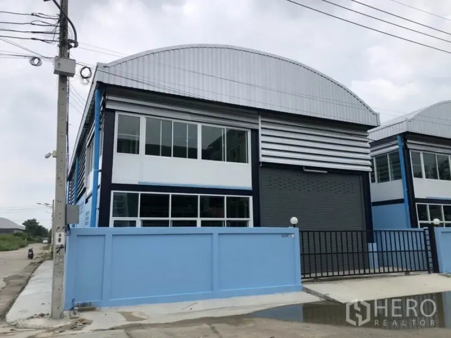 Factory for rent or sale in Bang Bua Thong, Nonthaburi - Modern factory exterior with blue wall, large roller shutter, and upper office windows.
