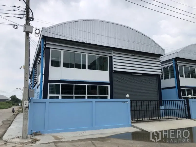 Factory for rent or sale in Bang Bua Thong, Nonthaburi - Modern factory exterior with blue wall, large roller shutter, and upper office windows.