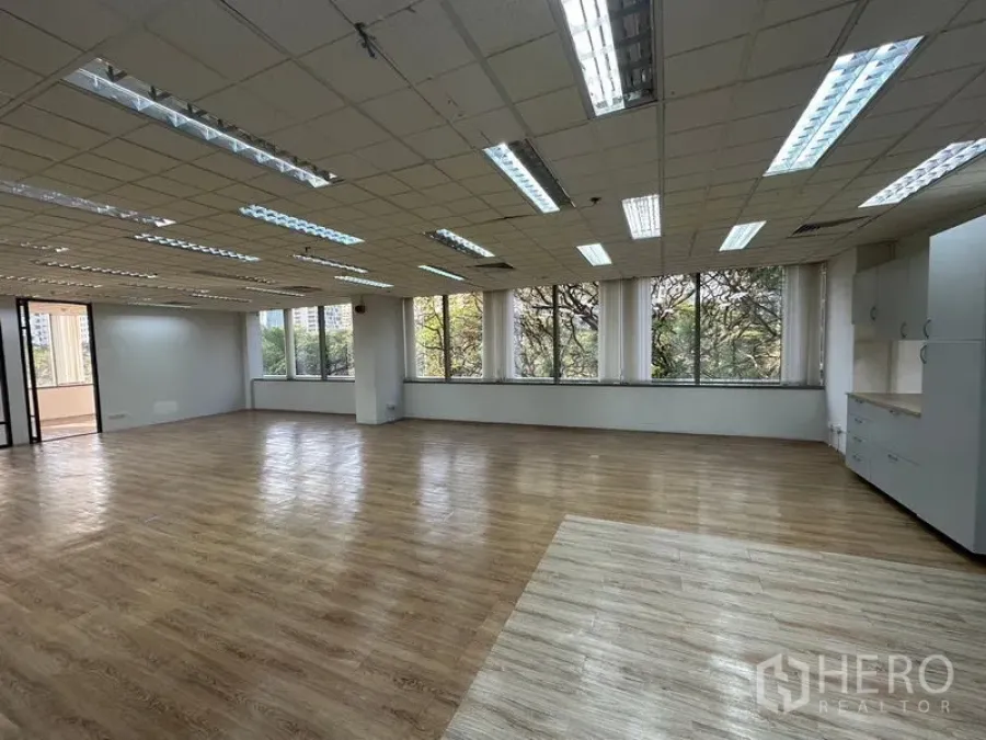 Office Space for rent - Spacious workspace with rows of windows, natural light, wood laminate flooring, and a built-in pantry cabinet.