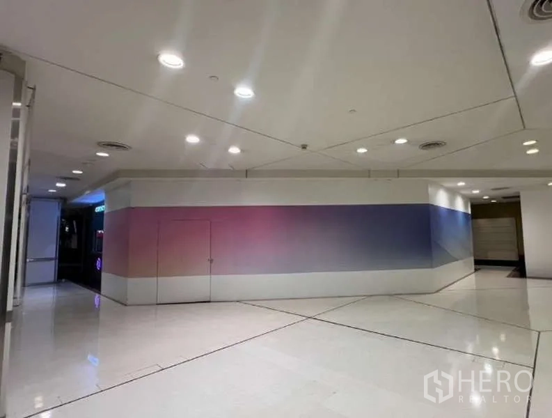 Retail Space for rent - Closed shopfront along a bright shopping passage with spotlights and wide frontage, ideal for signage and high visibility.